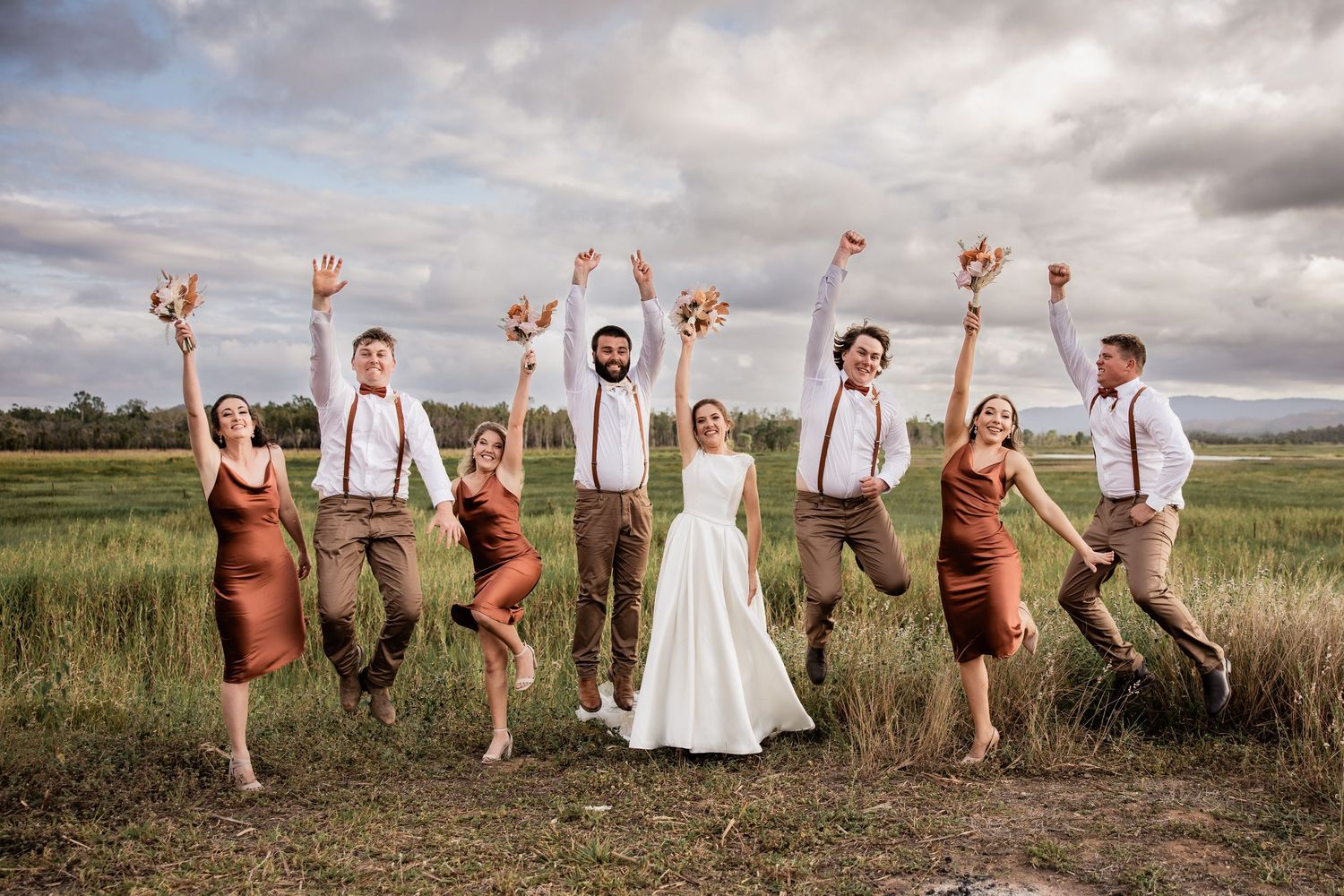 Wedding party jumping with joy in a rustic field setting.