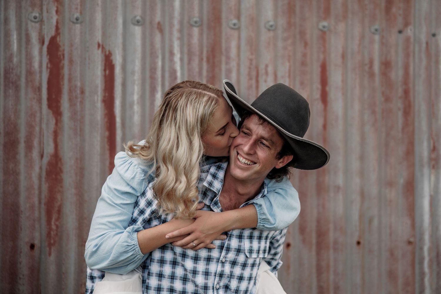 A playful couple sharing a joyful moment against a rustic metal wall background.
