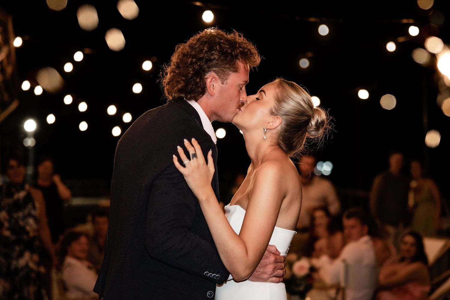 A romantic wedding dance moment under twinkling lights at an evening reception.