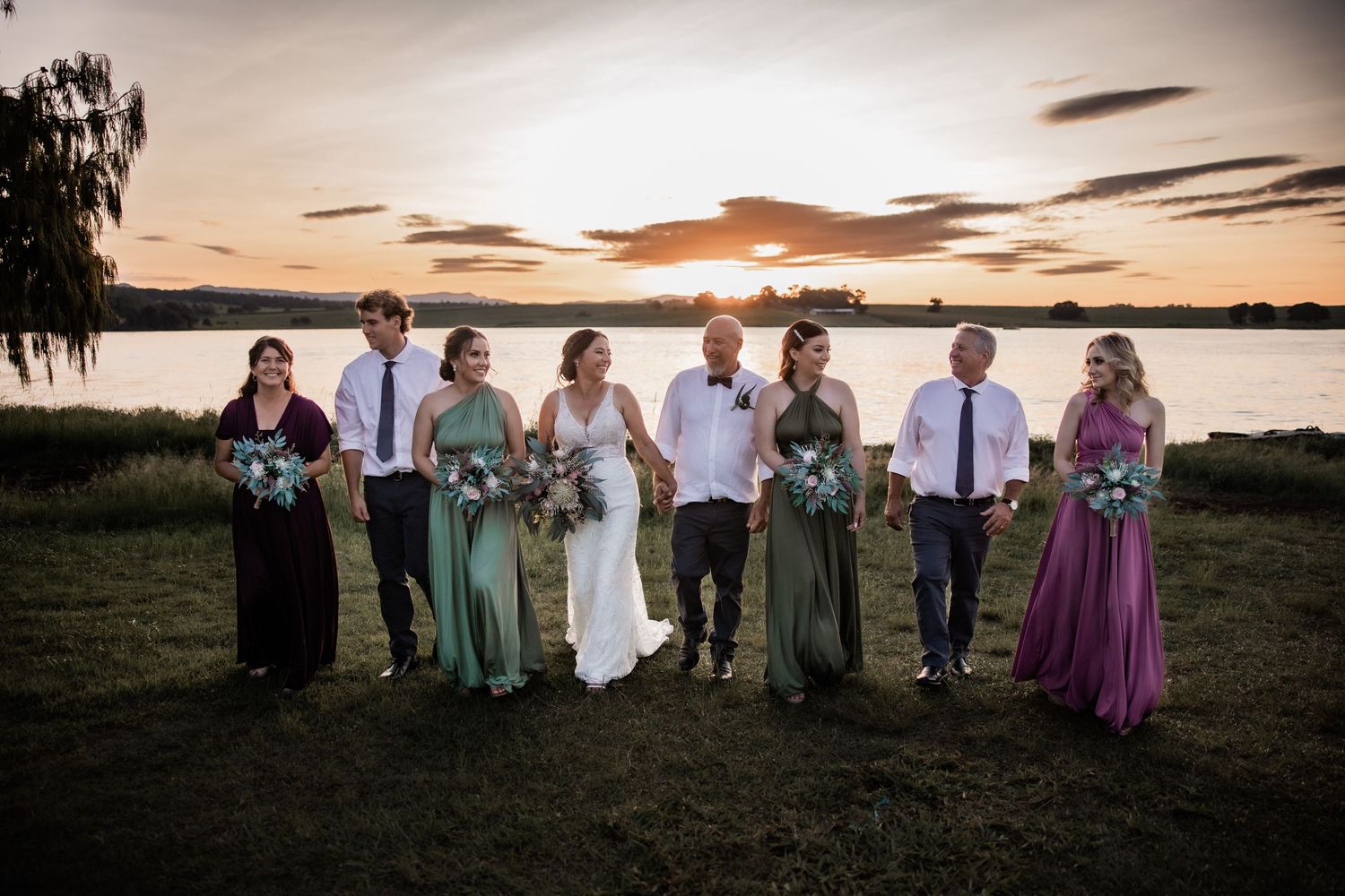 Wedding party poses by lakeside during golden hour sunset.