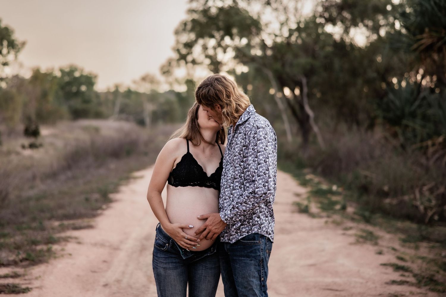 A couple shares an intimate moment on a dirt path during sunset.