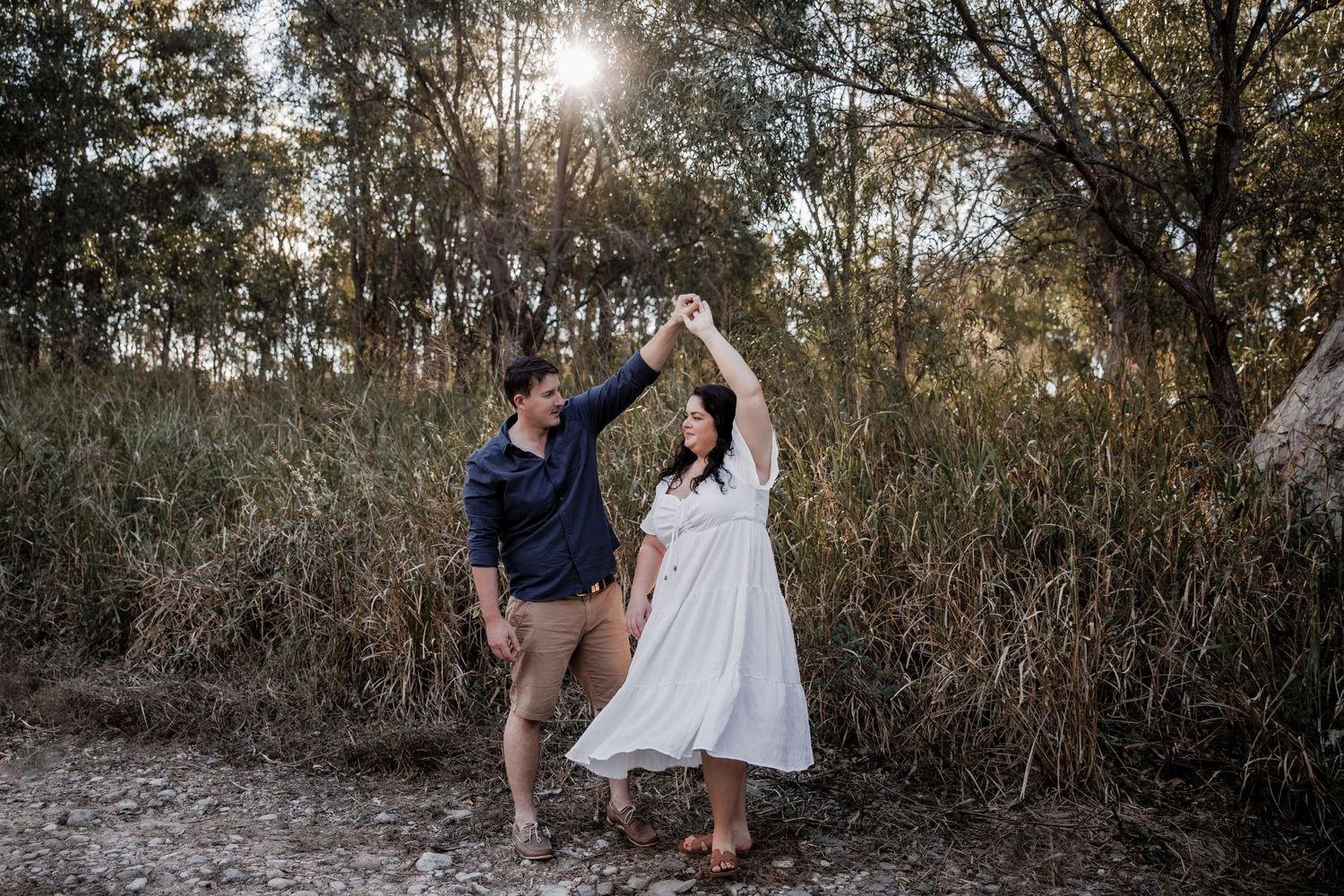 Couple dancing together on nature trail with sunlight streaming through trees.