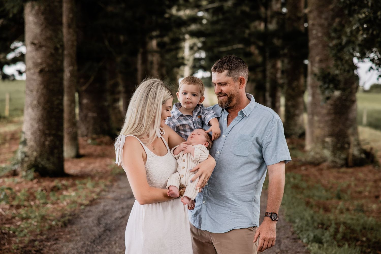 A family of three posing together on a tree-lined path during a photo session.