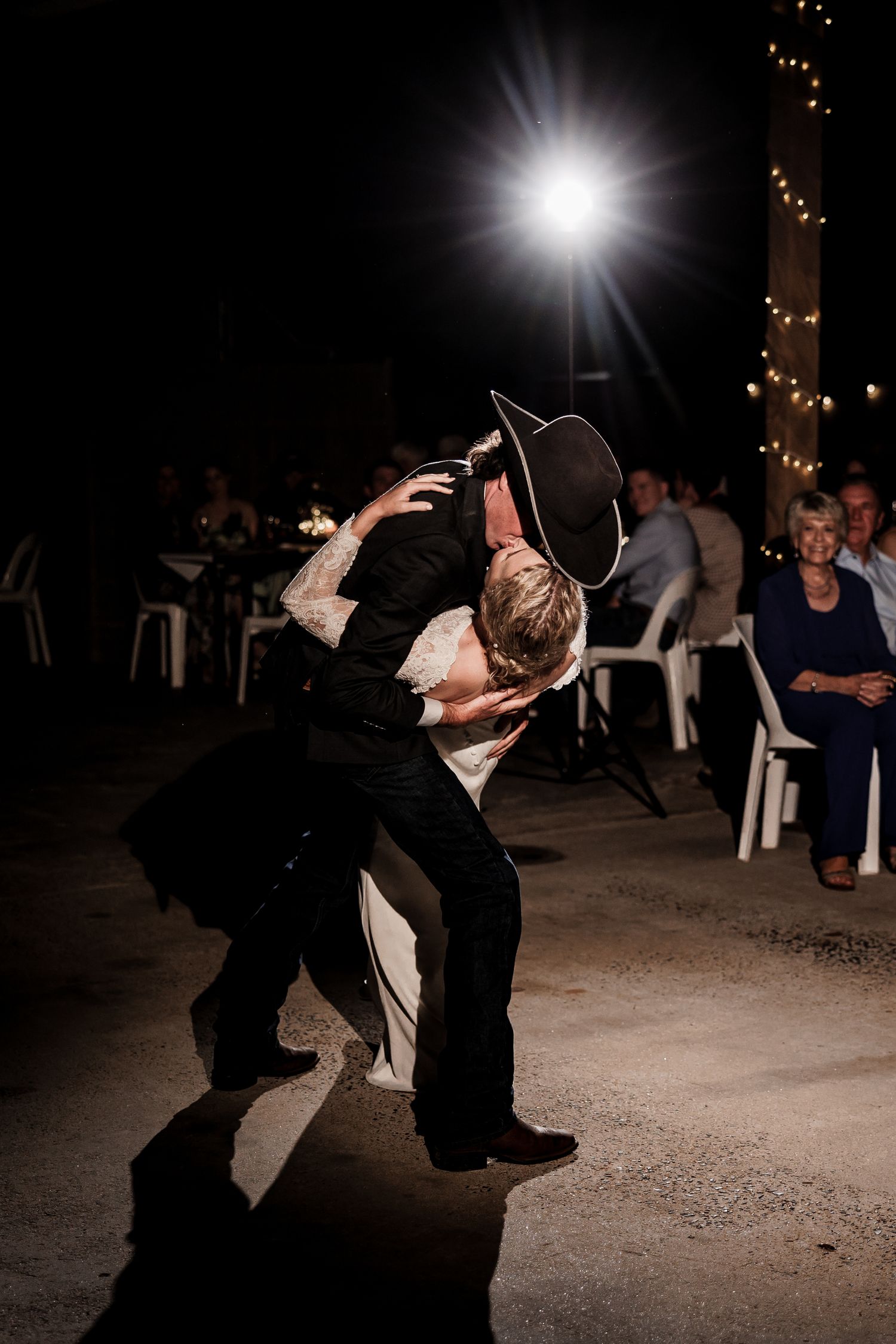 A dramatic dance move captured at a wedding reception with string lights glowing in the background.