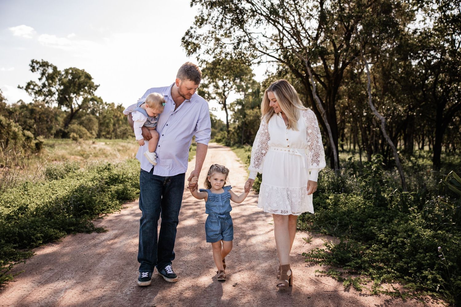 A family walking together on a dirt path through bushland during golden hour.