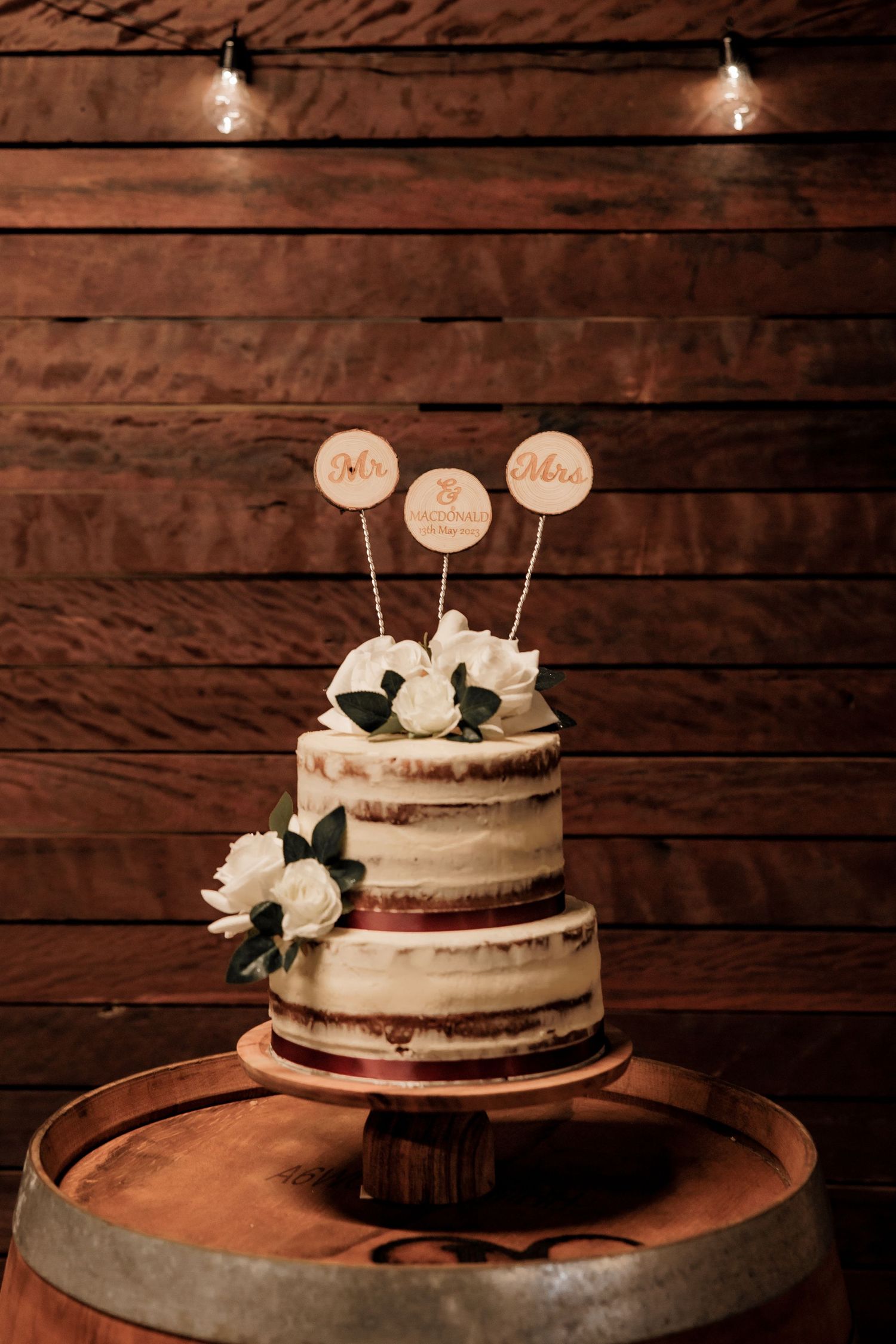 A rustic semi-naked wedding cake with floral decorations displayed on a wooden barrel.