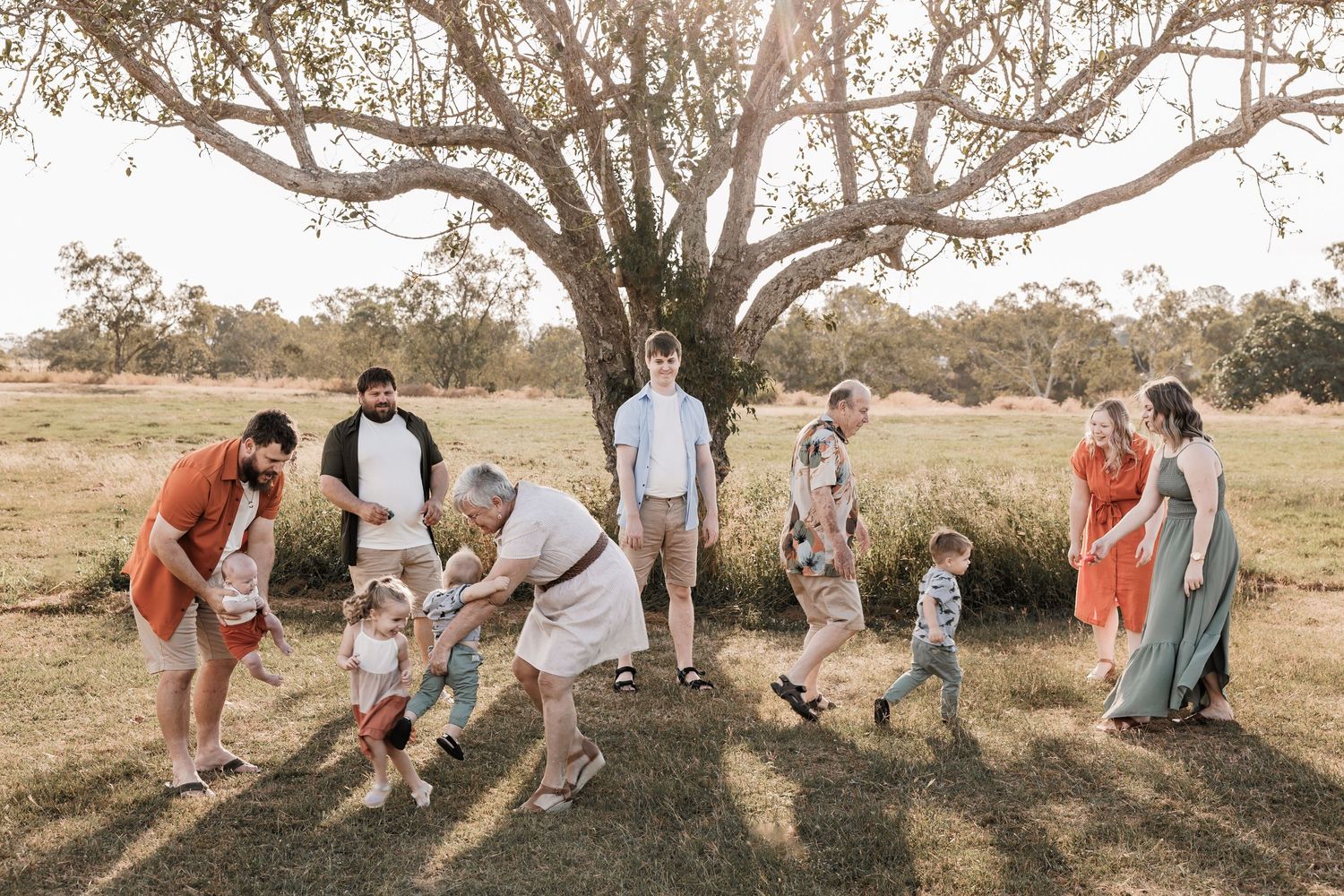 Extended family gathers for a playful photo under a grand tree in an Australian field.