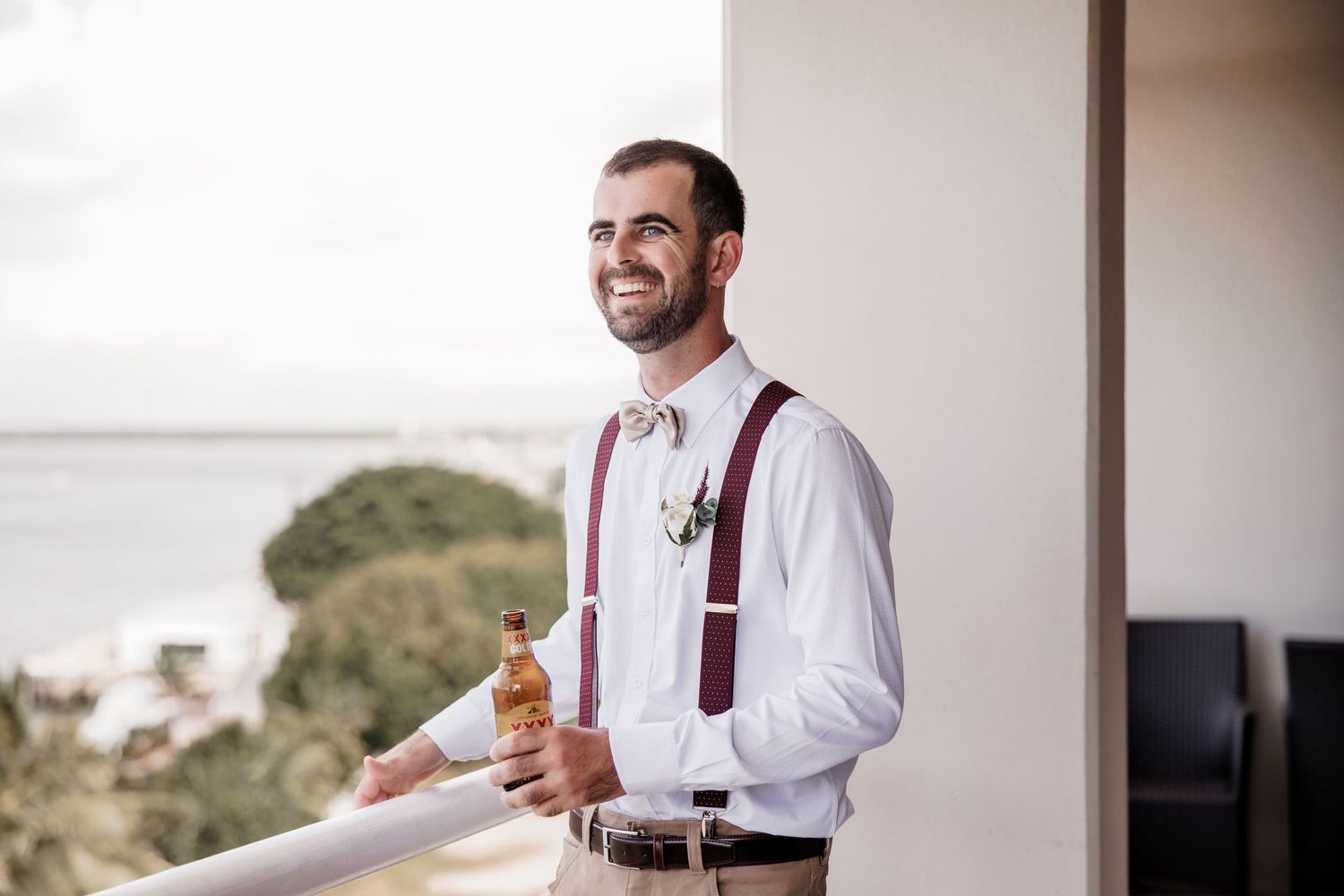 Person in white shirt and suspenders smiling while holding a drink outdoors.