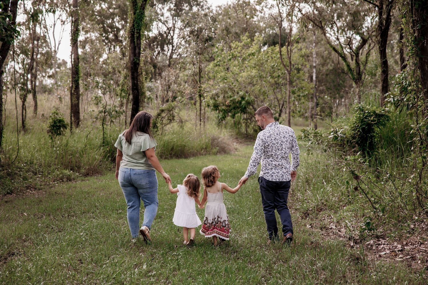 A group walks together holding hands along a wooded path during an outdoor family photo session.