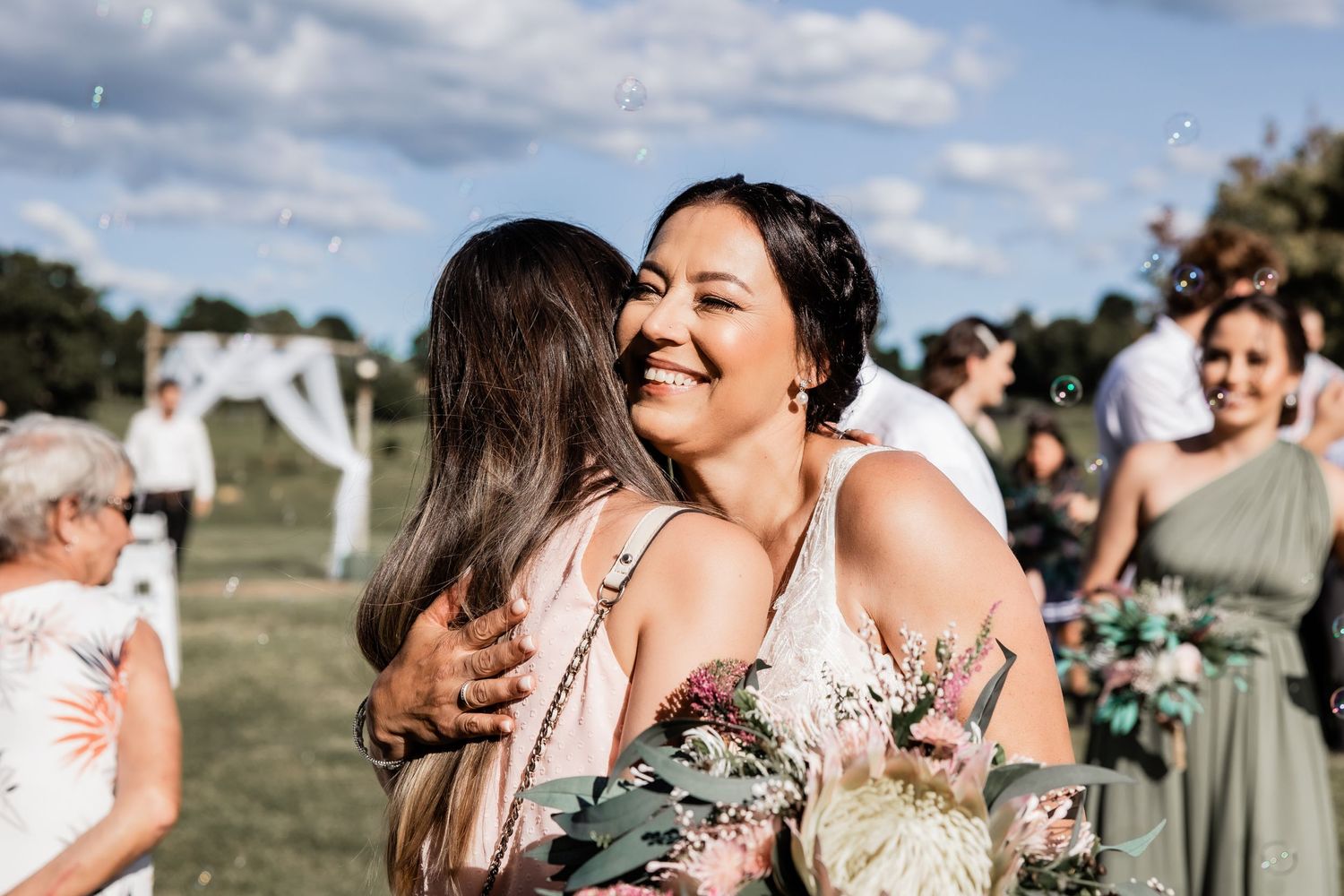 Wedding guests share joyful hugs during outdoor celebration.