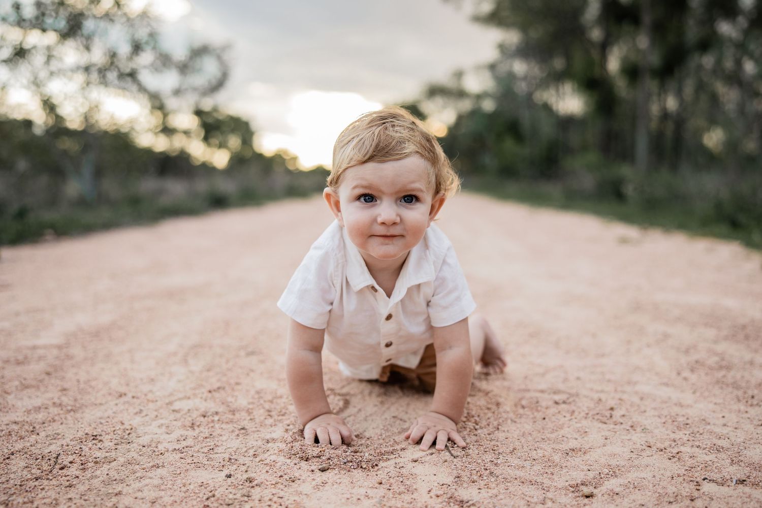 Small child crawling on a rustic dirt road during golden hour.