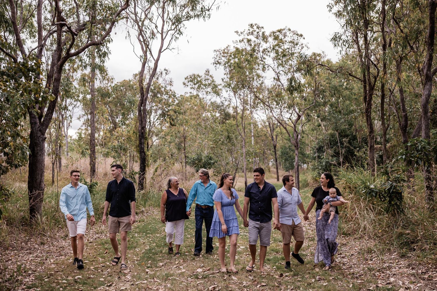 A group walks together through a wooded area during a casual outdoor photoshoot.