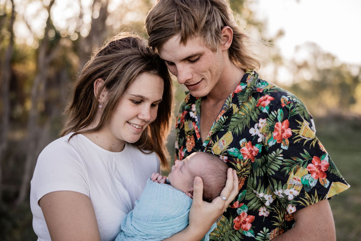 A couple shares an intimate moment with their baby during an outdoor portrait session.