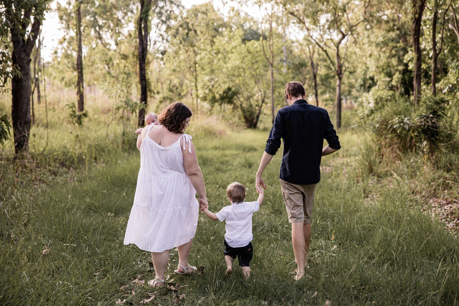 A family walks hand in hand through a sunlit forest clearing during golden hour.