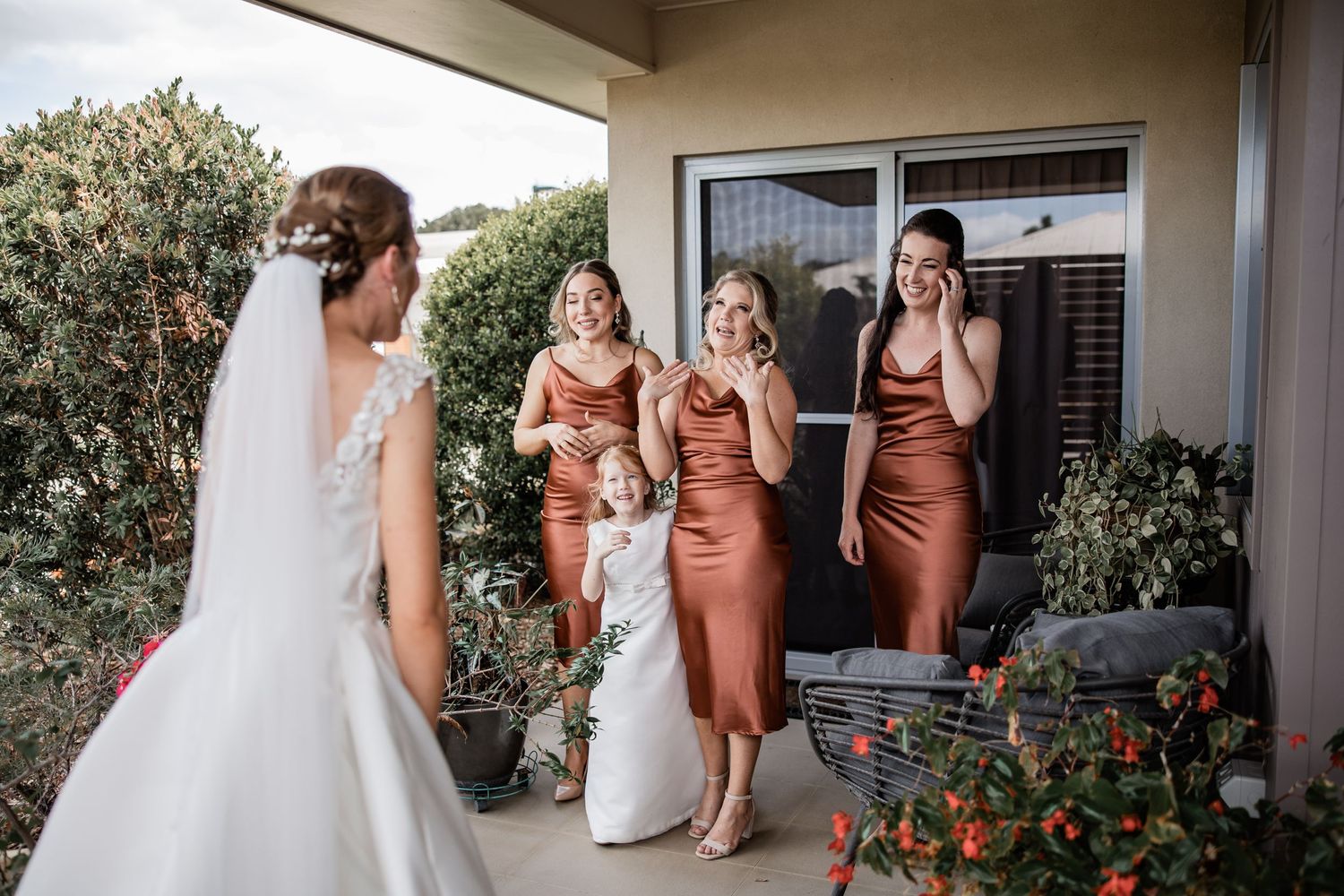 Wedding party having a joyful reaction on an outdoor patio with potted plants.
