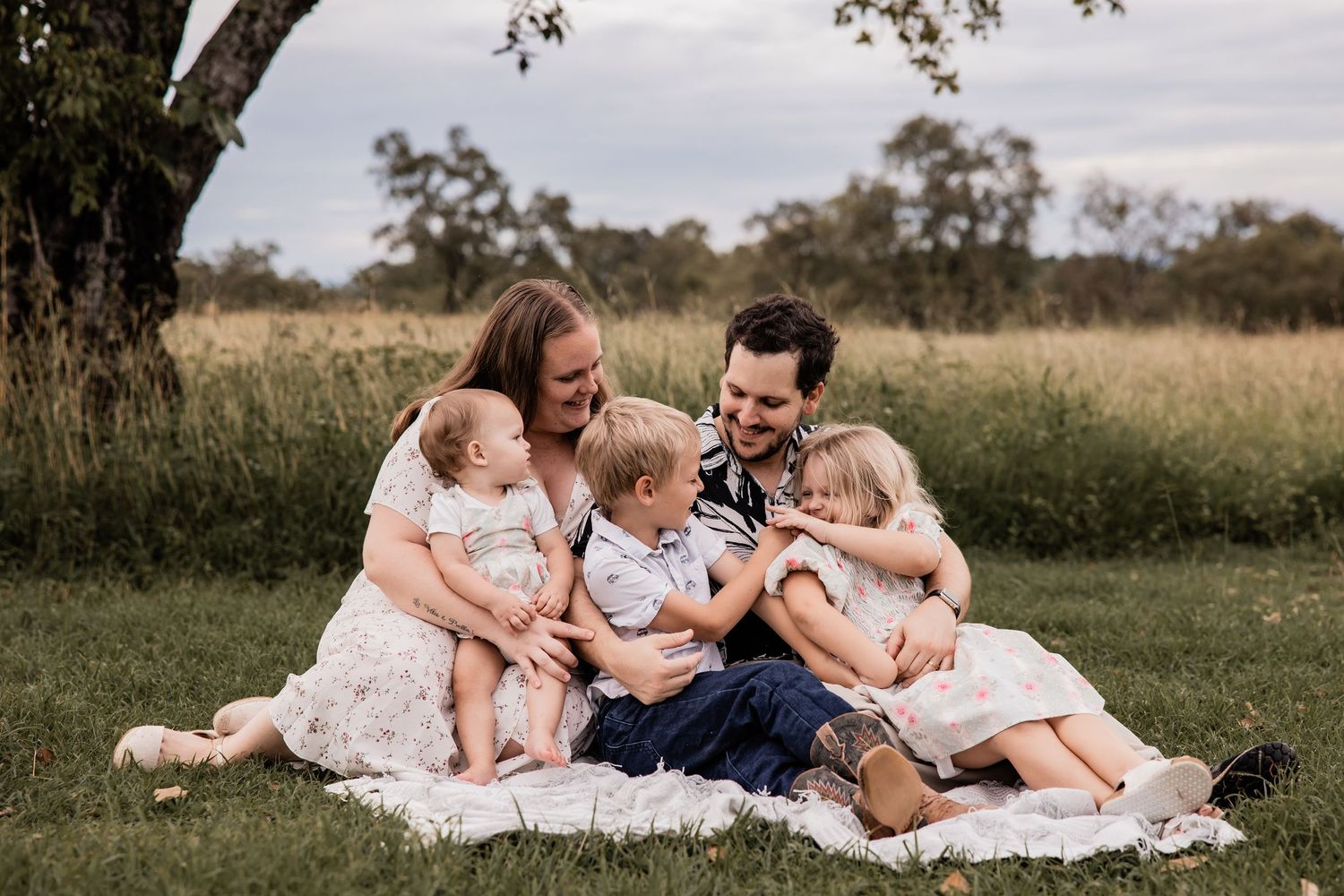 A family shares intimate moments while sitting together on a blanket in a field.