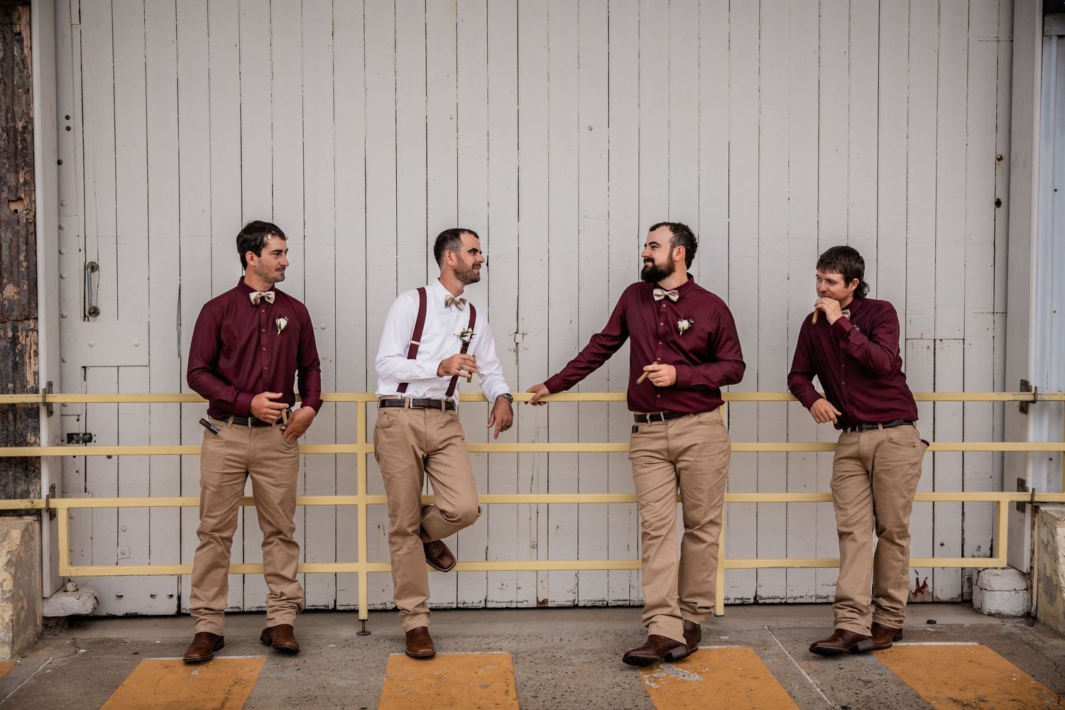 Groomsmen perform synchronized dance moves against white barn wall.