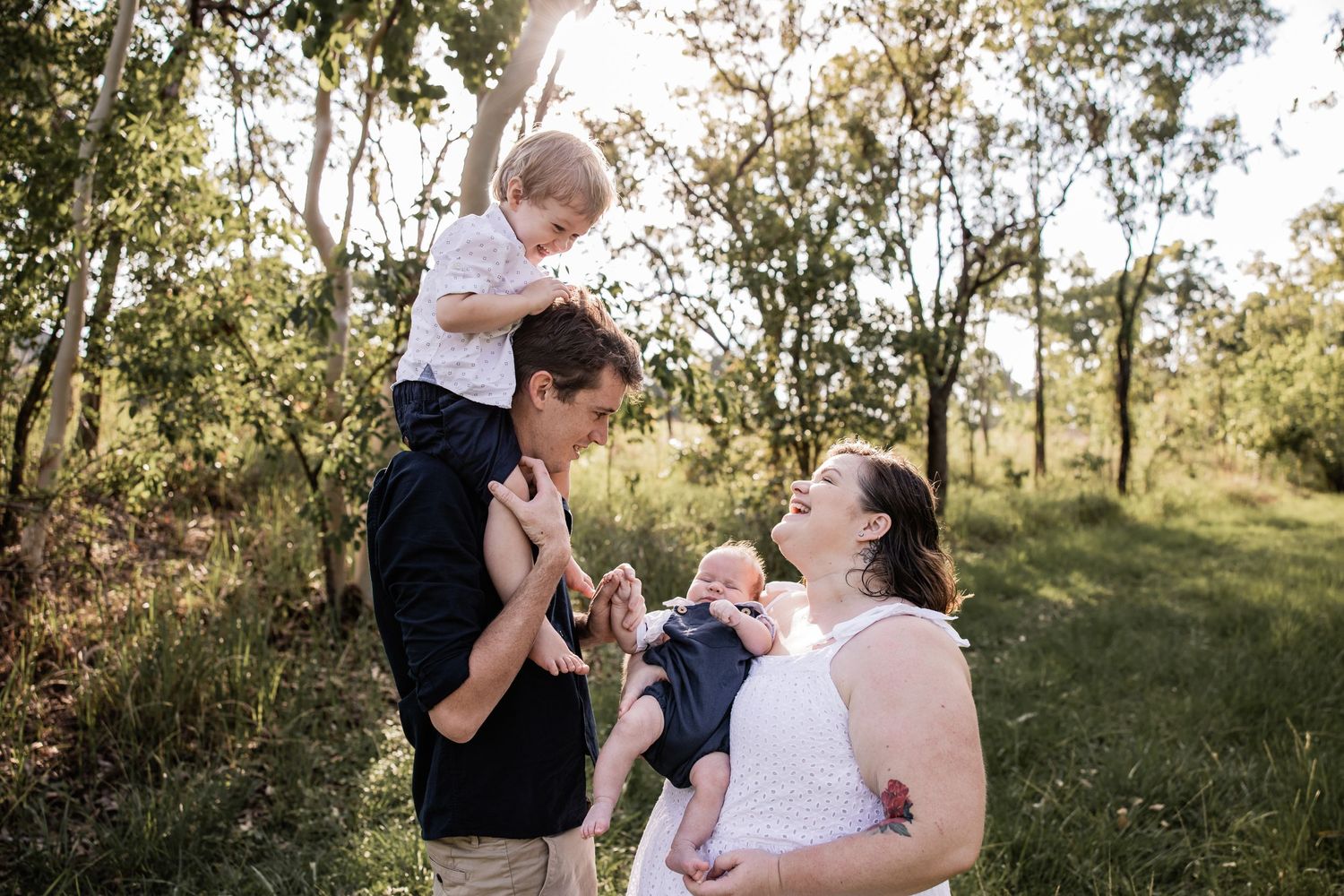 A sweet family moment captured outdoors with natural light filtering through trees in the background.
