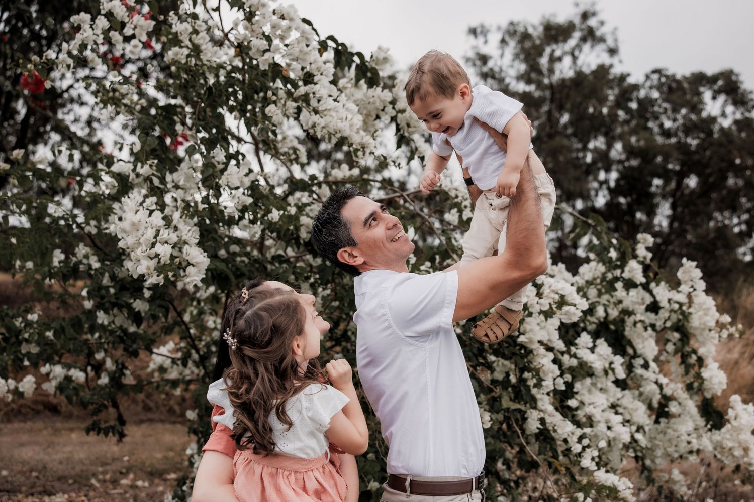 A father lifting a small child in the air amidst blooming white flowers.