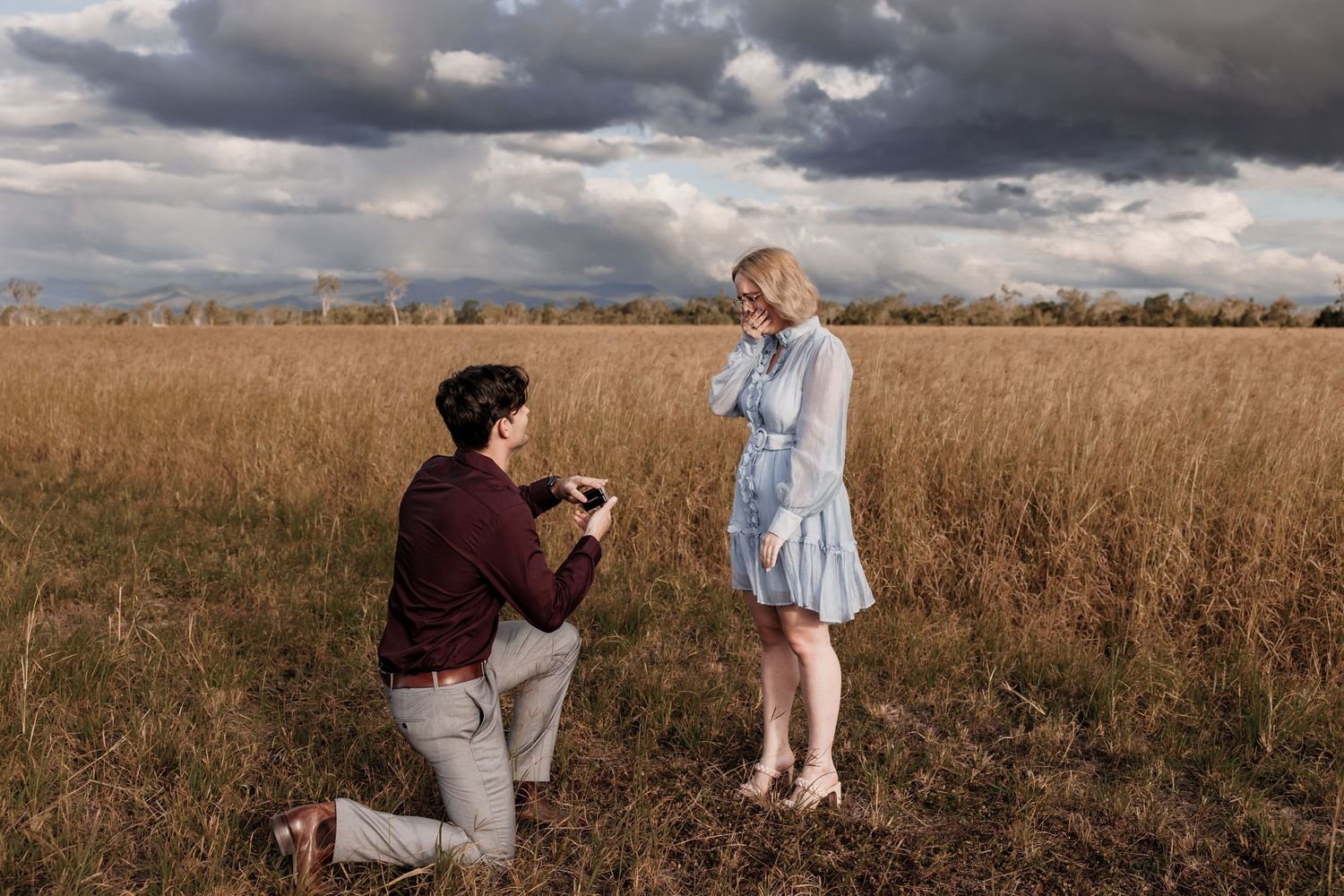 Marriage proposal scene in a golden field with dramatic storm clouds overhead.