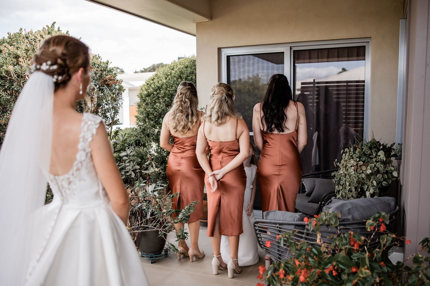 A wedding party gathering on a patio with terracotta colored bridesmaid dresses.