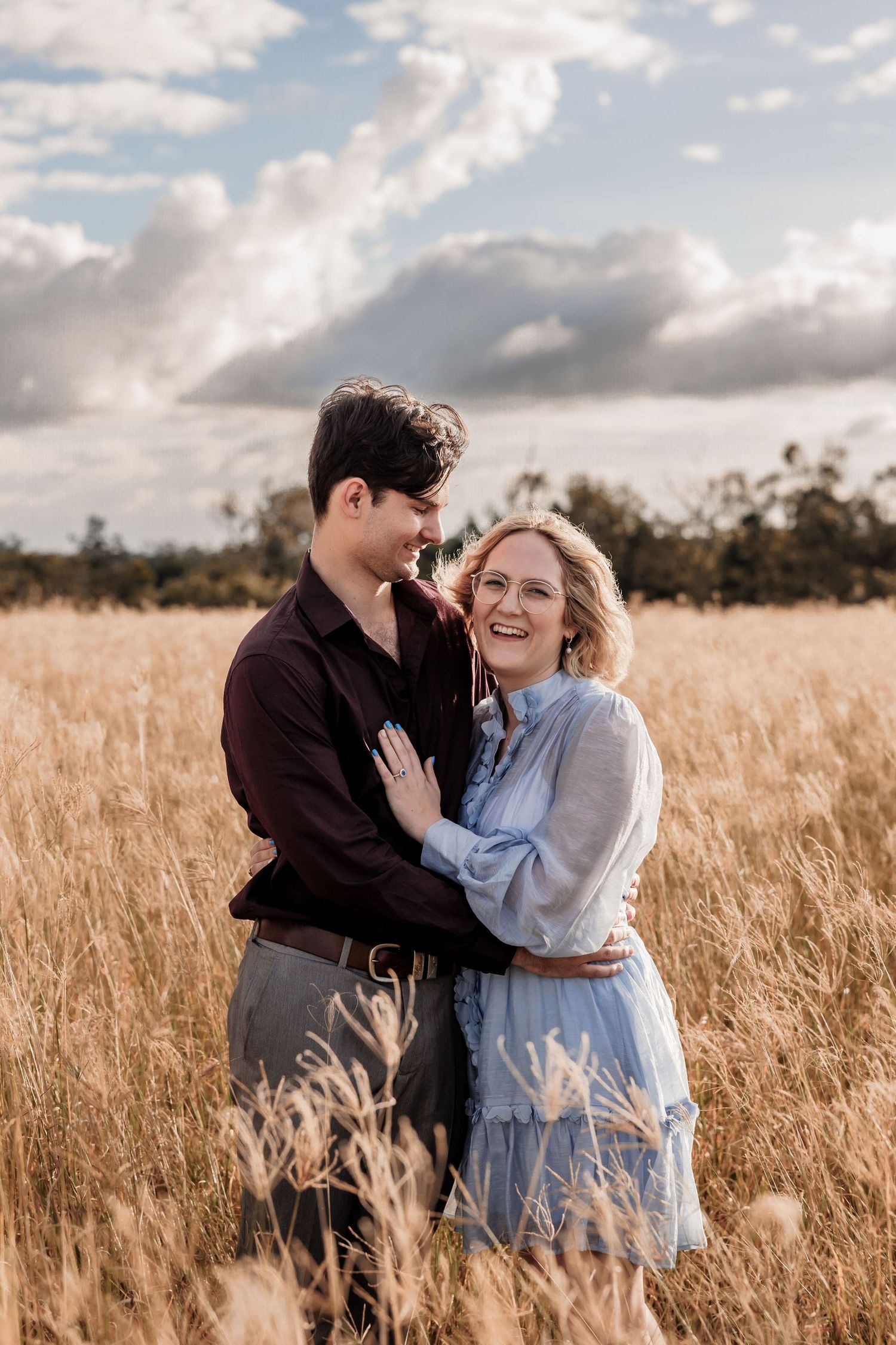 Couple sharing an intimate moment in a golden wheat field under cloudy skies.