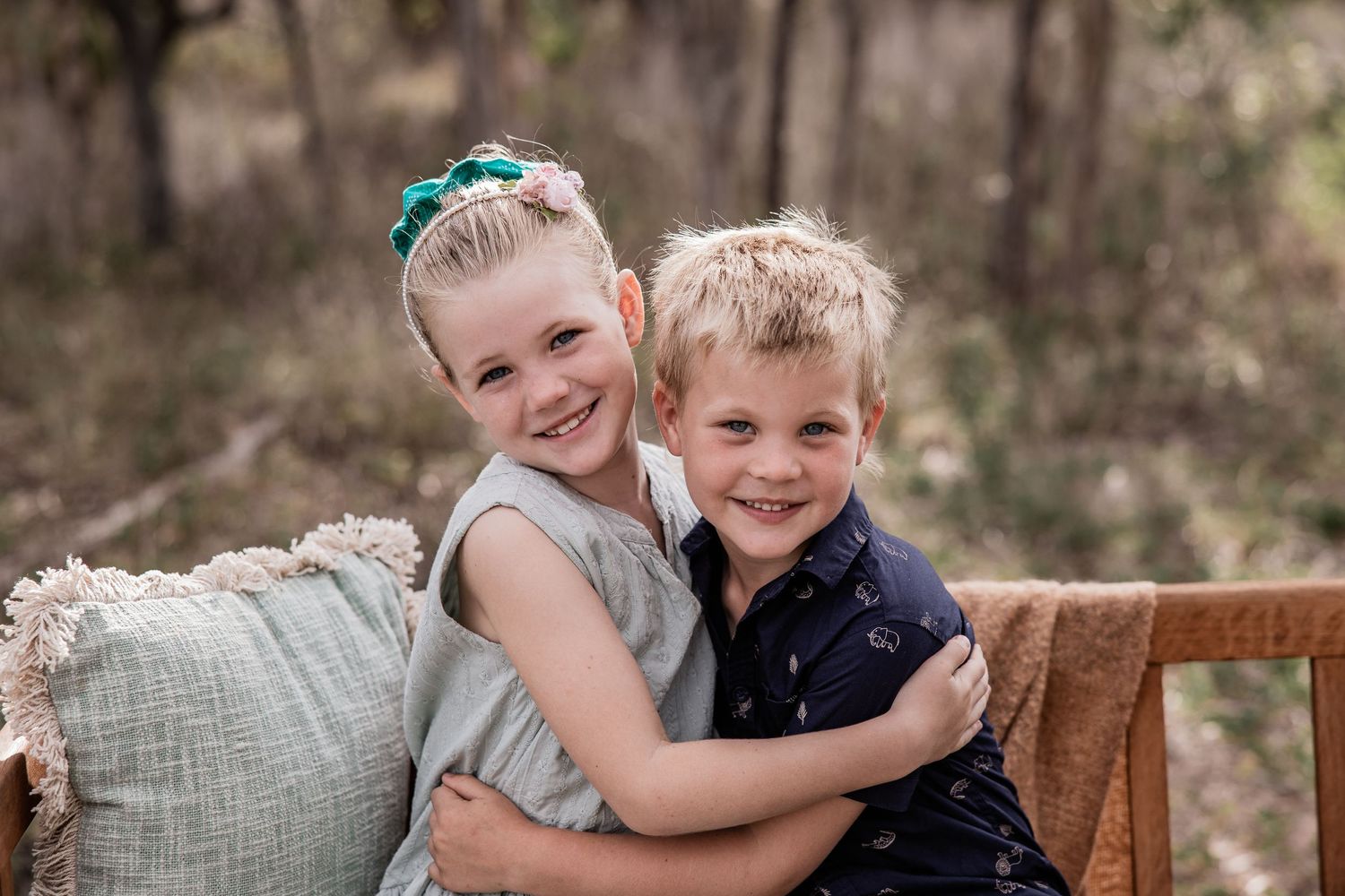 Two children embrace on cushioned bench during outdoor portrait session.