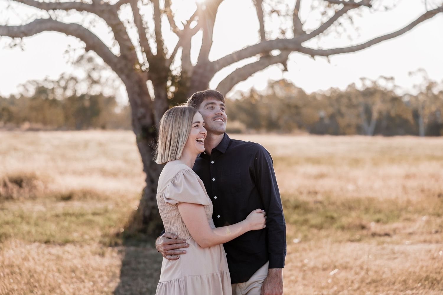 A tender romantic moment captured between two people under a large tree at sunset.
