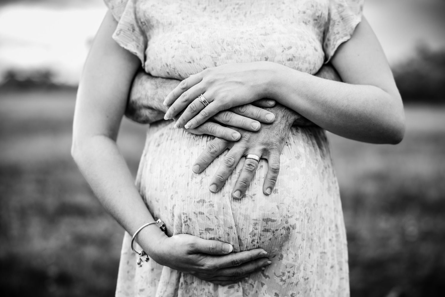 Hands rest gently on a growing belly shown in black and white.