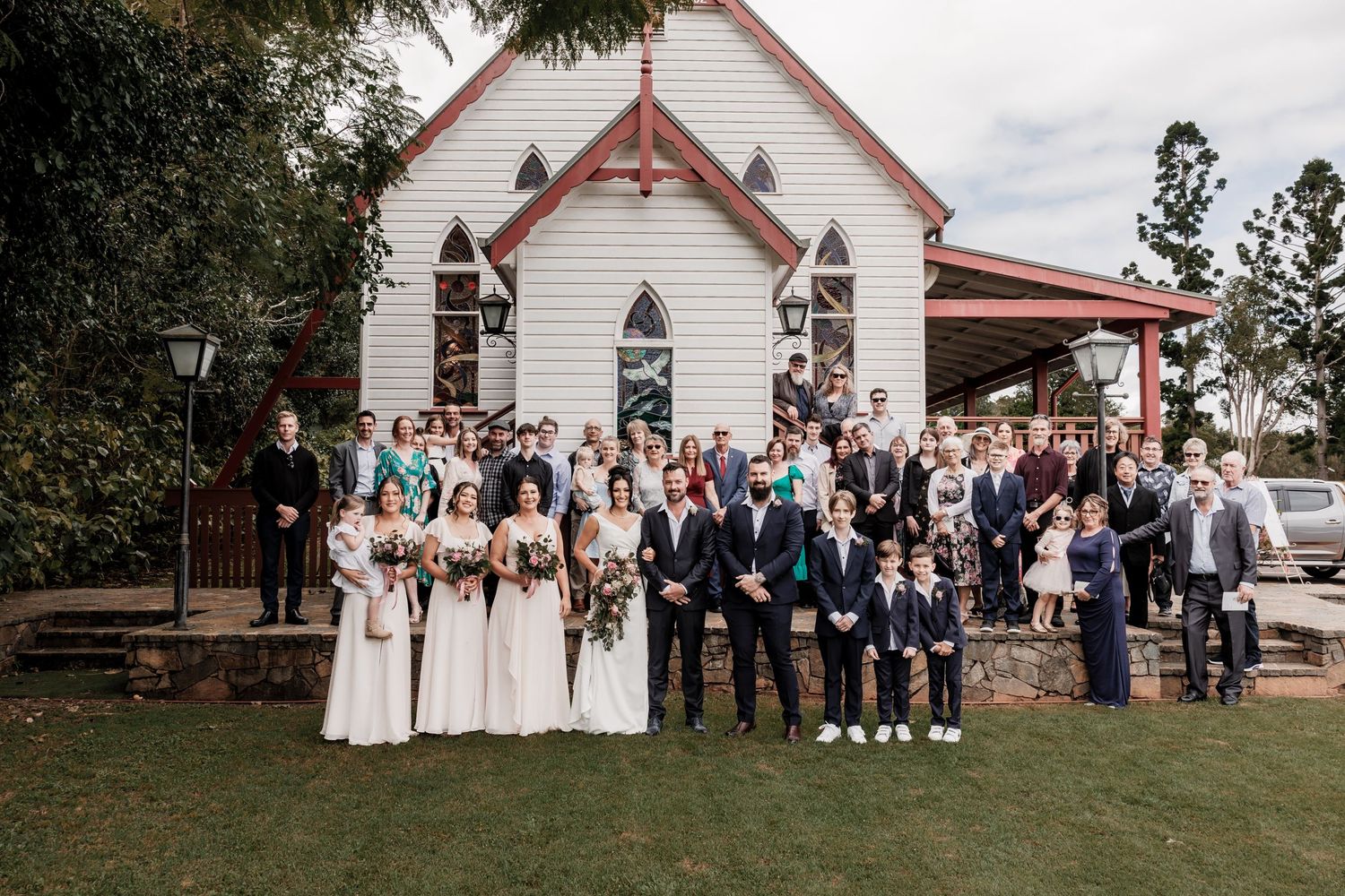 Large wedding party group photo in front of a charming white chapel.