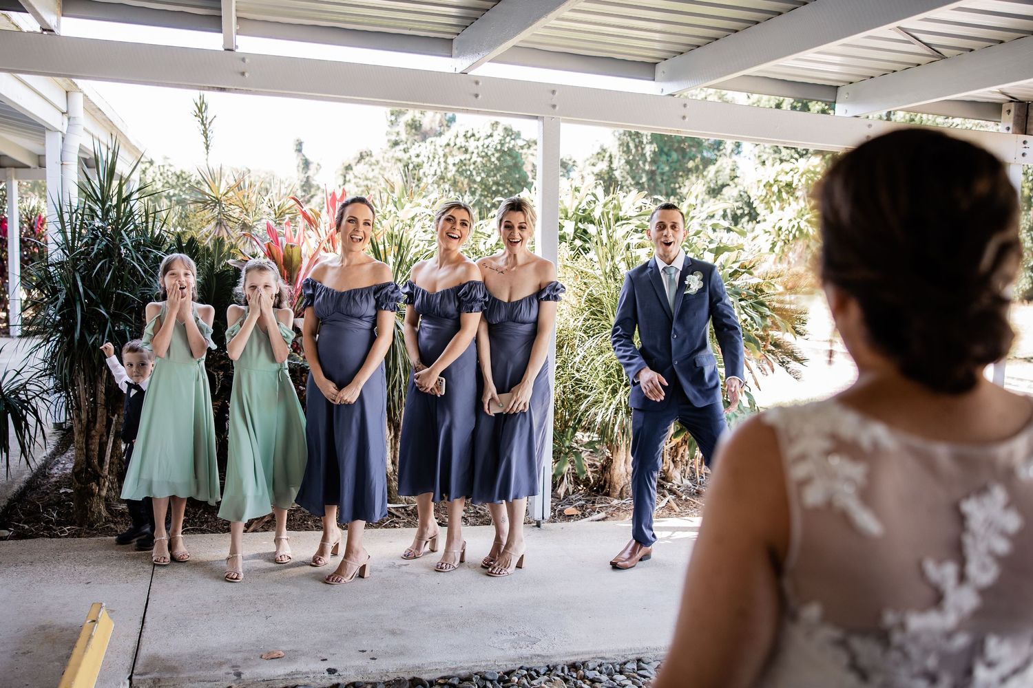 Wedding party in mint green and navy dresses gathered on a covered outdoor terrace.