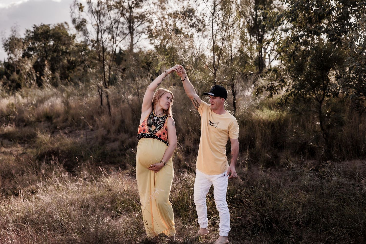 A couple dances together on a dirt path surrounded by trees at golden hour.