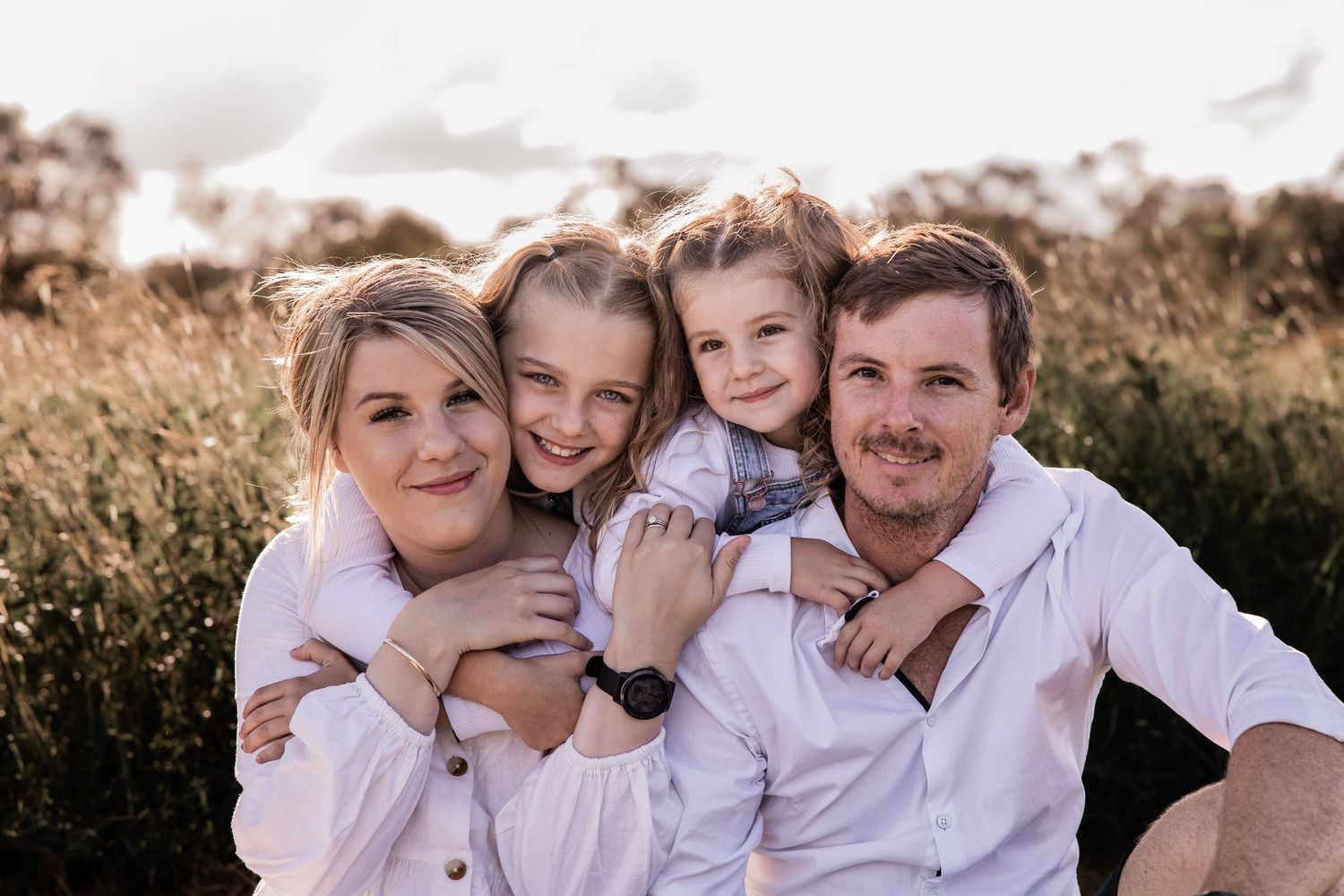 Family poses together in tall grass during golden hour portrait session.