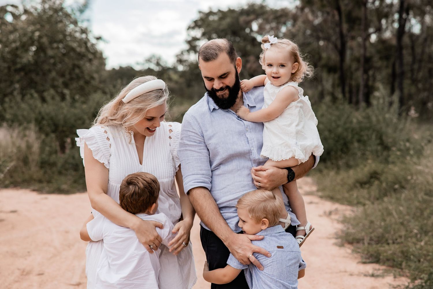 A family of five poses together on a rustic dirt path surrounded by trees.