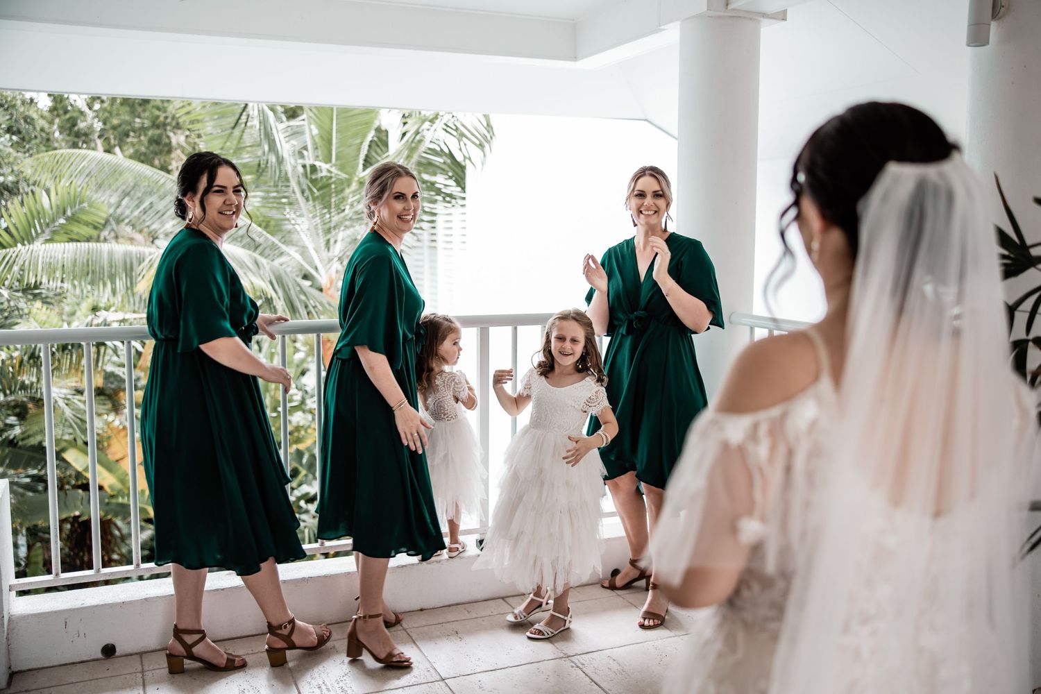 Bridesmaids in emerald green dresses react to seeing the bride in her wedding gown.