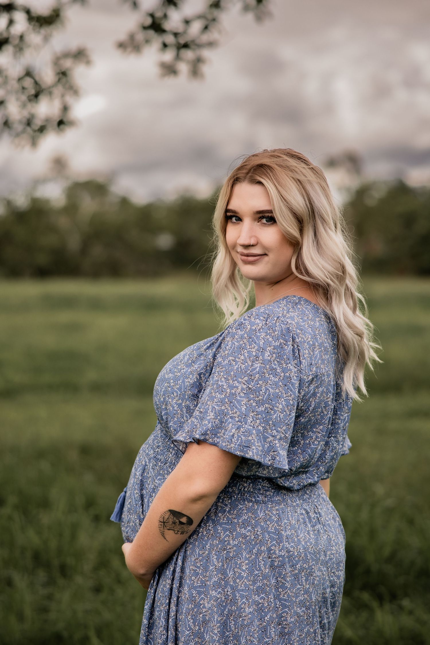 A floral patterned dress highlights a baby bump in an outdoor maternity photo.