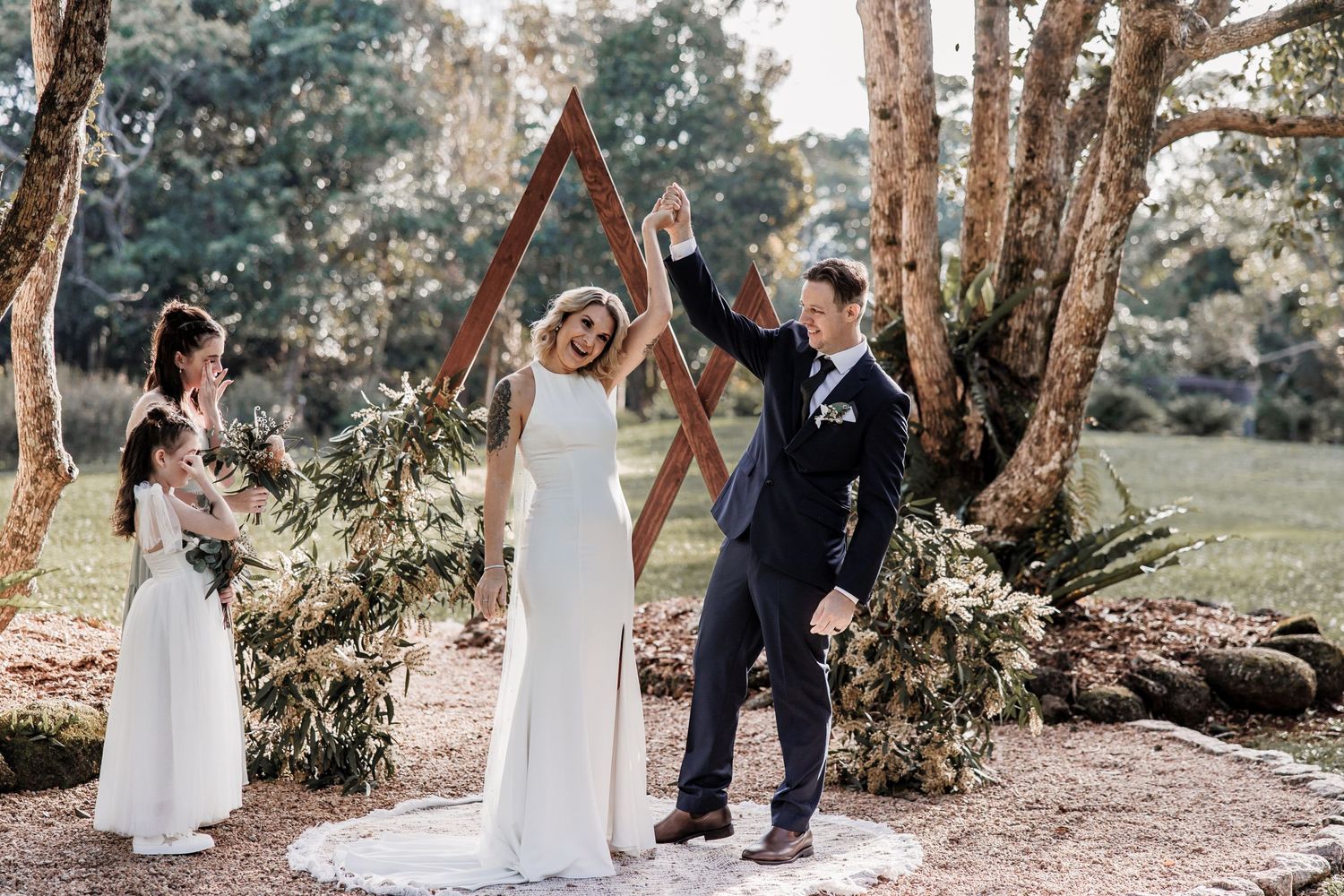 Wedding celebration in a forest setting with wooden triangular arch.