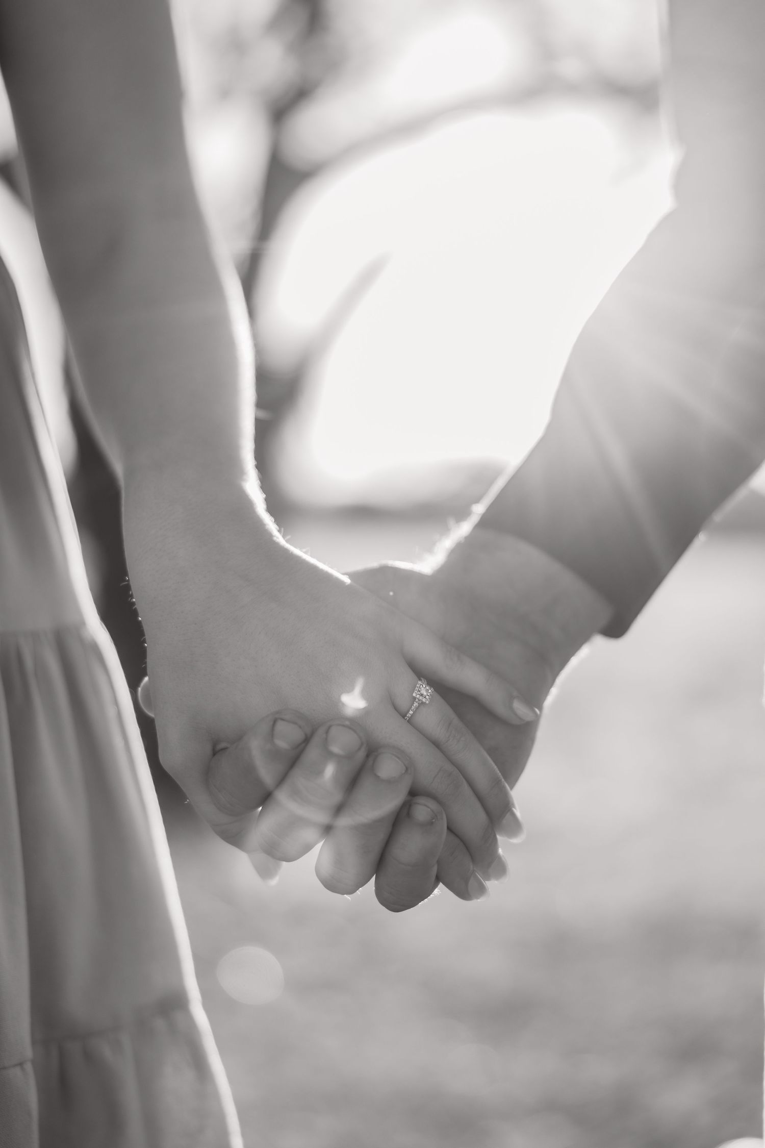 Close-up black and white photo of two people holding hands with sunlight streaming through.