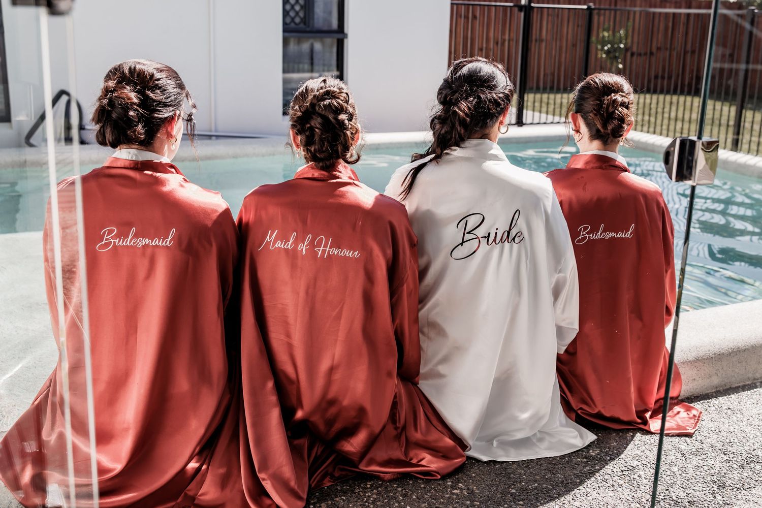Group wearing matching silk robes in coral and white colors sitting by a pool.