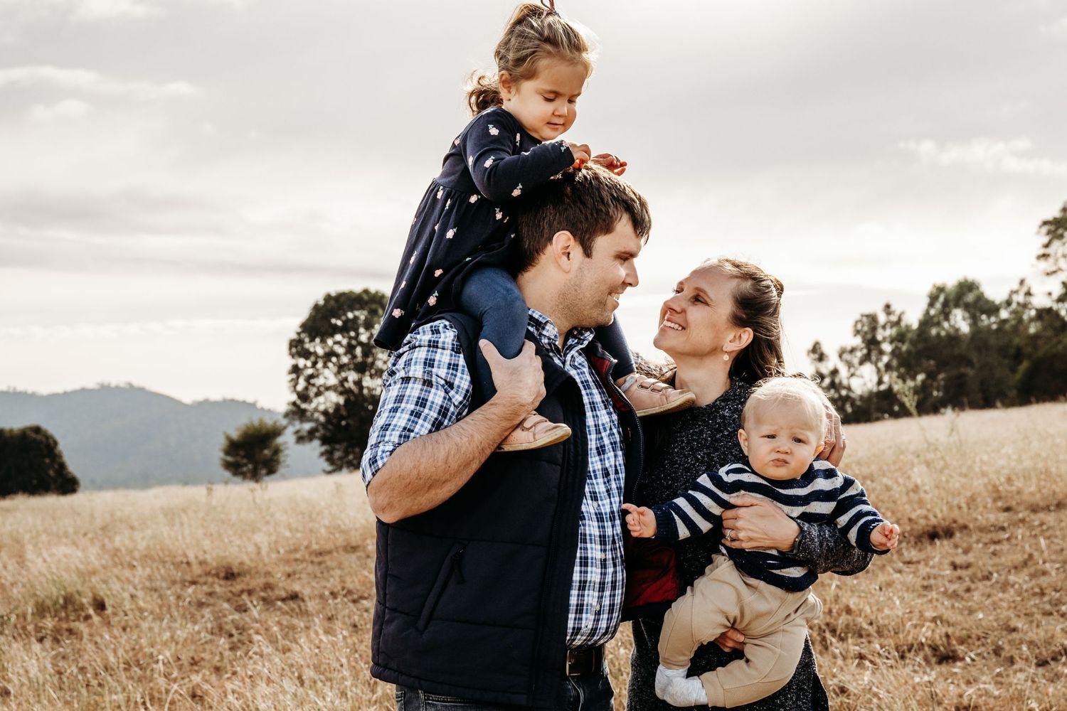 A joyful family moment captured in an open field with mountains in the background.