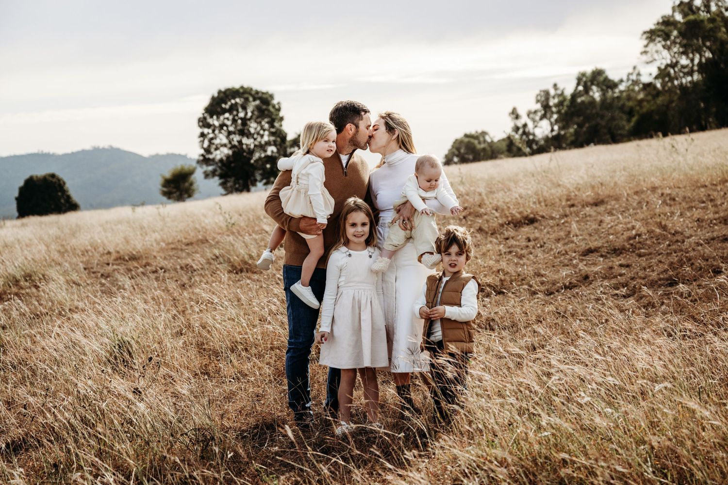 A family portrait taken in a hilltop meadow with mountains visible in the distance.