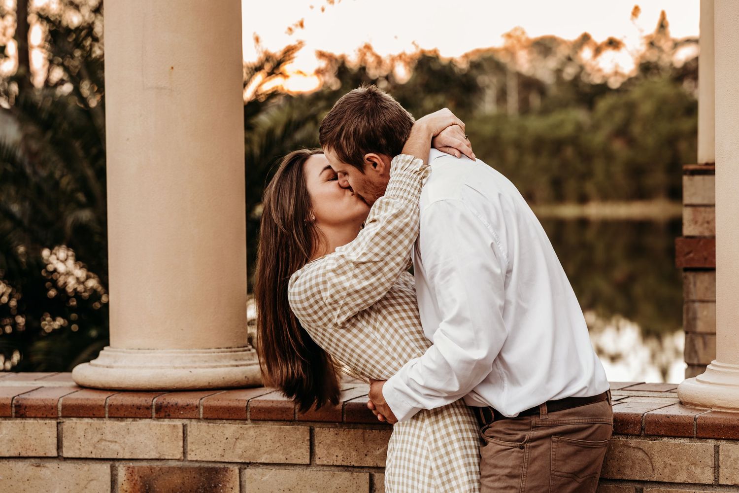 Romantic couple sharing an intimate moment against a sunset backdrop with white columns.