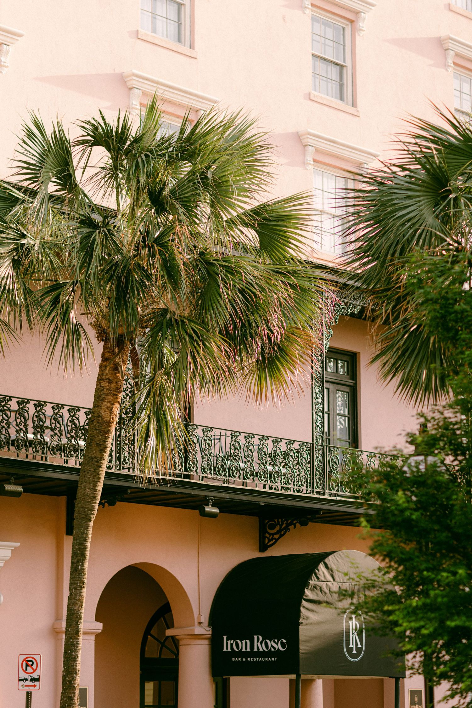 Pink historic building with wrought iron balcony and palm trees in Charleston style architecture.