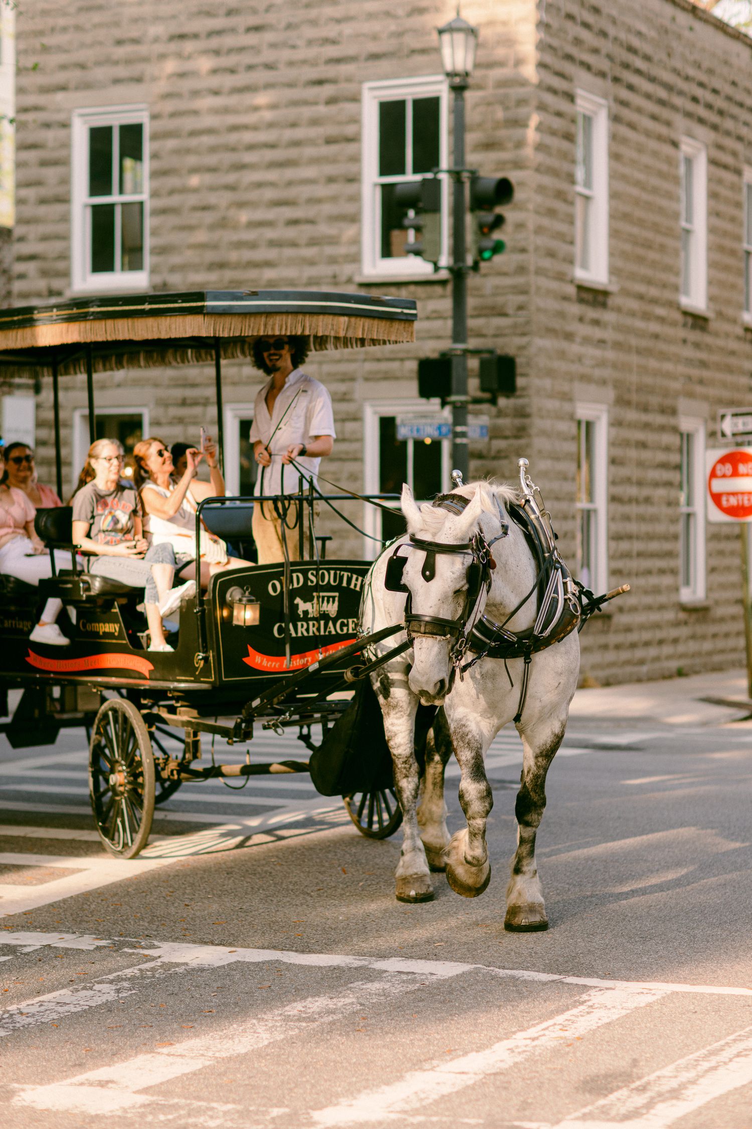 A white horse pulls a traditional carriage through historic streets with brick buildings and a stop sign in view.