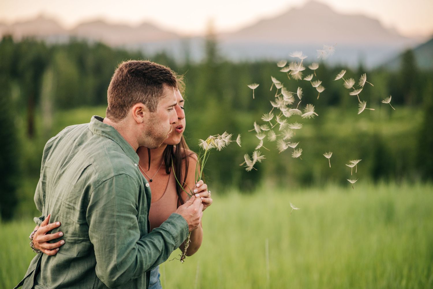 A tender embrace while blowing dandelion seeds in a mountain meadow at sunset.