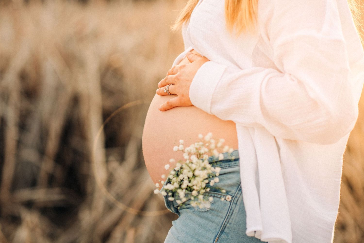 Image of a pregnant woman bump with baby breath flowers tucked into the mother jeans pocket