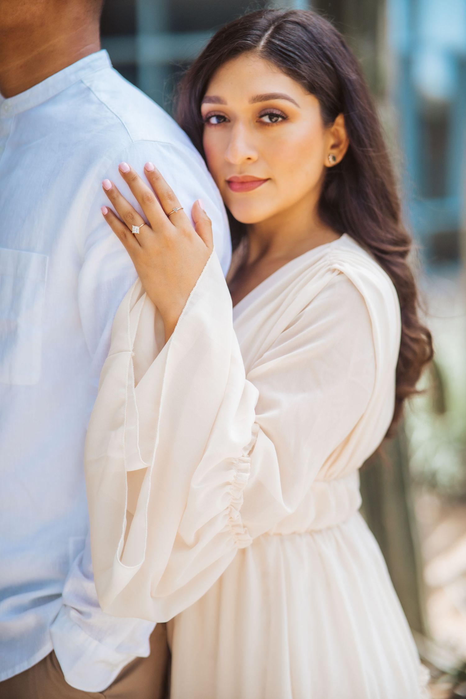 Woman in white dress poses elegantly showing engagement ring during romantic photoshoot.