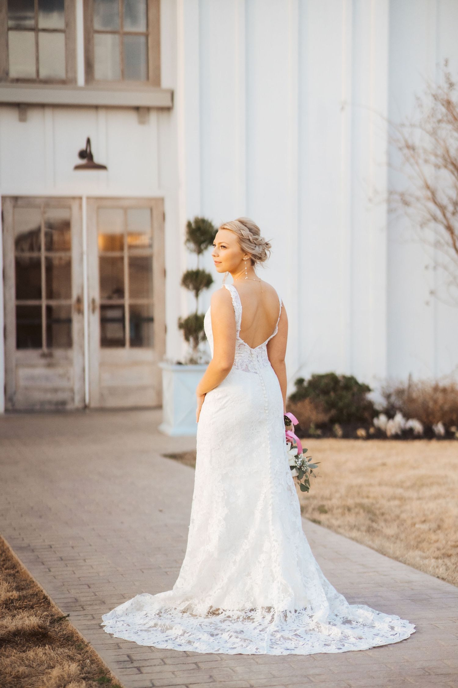 Back view of bride in fitted lace gown with long train outside white building.