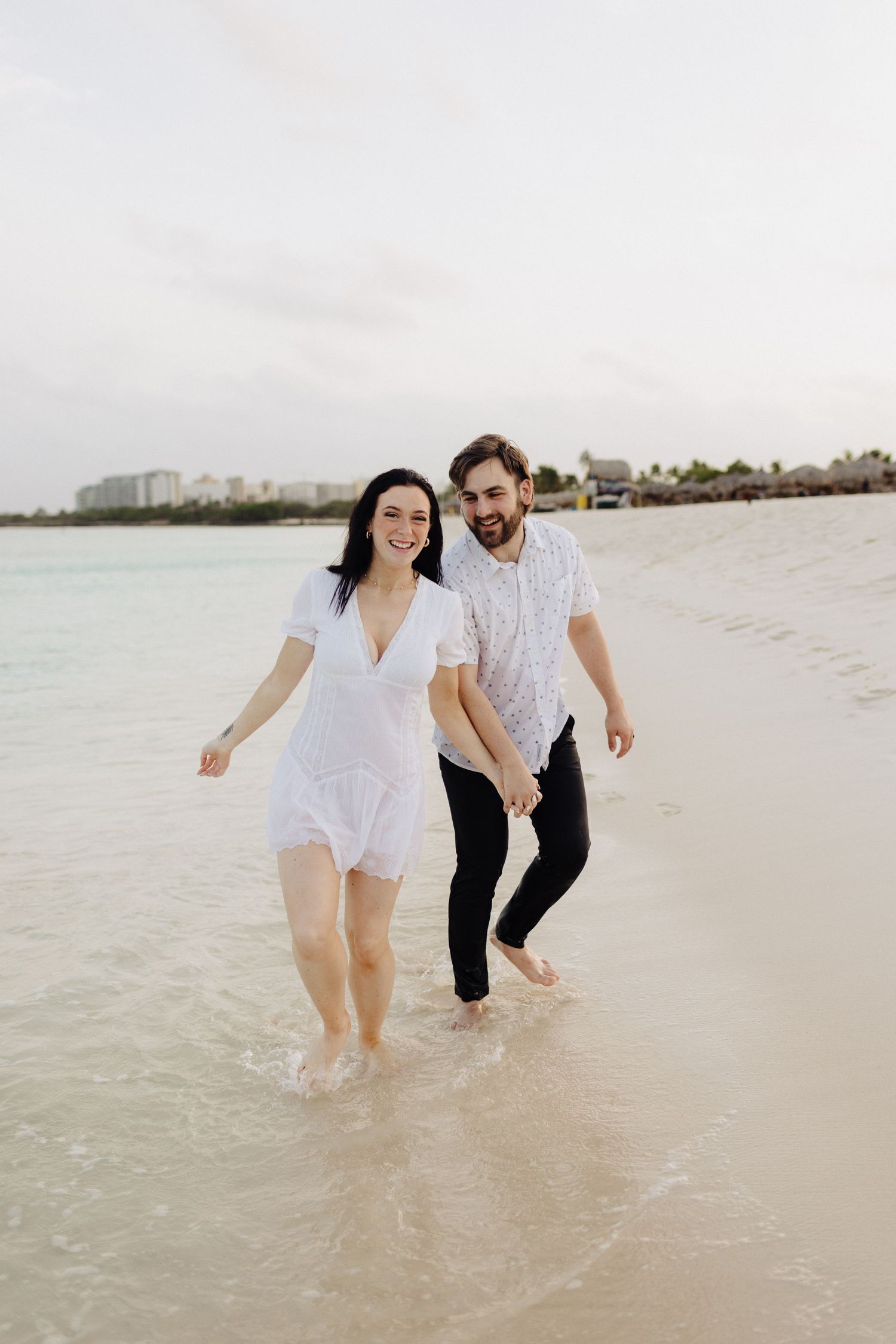 A joyful couple splashing in shallow water along a tropical beach at sunset.