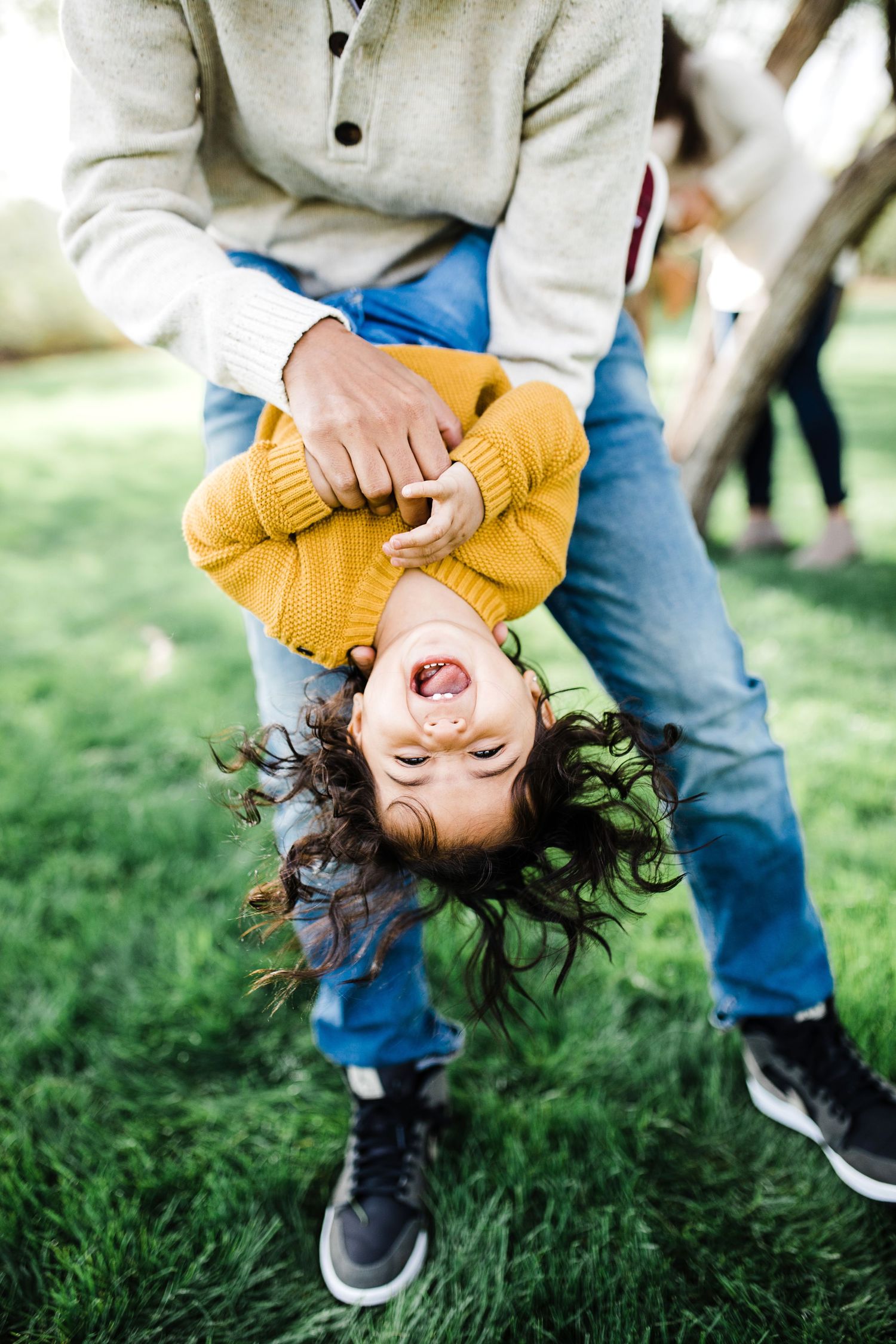 Laughing child held upside down by parent on green grass during outdoor family playtime.